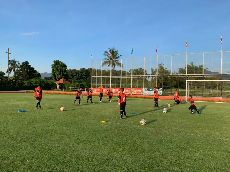 A squad in orange kit working through ball drills near the goal
