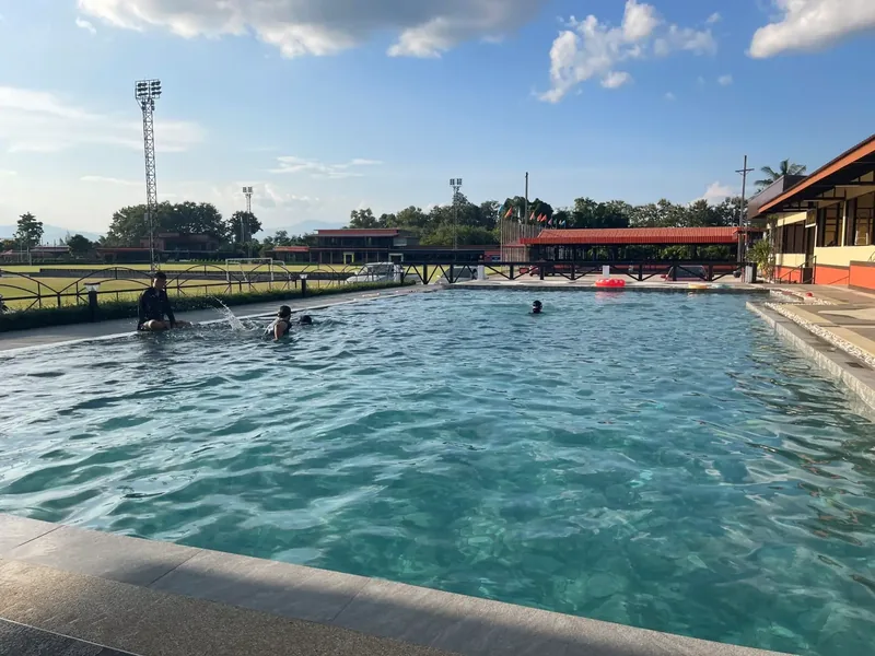 Guests swimming in the resort pool, with the pitch and floodlight towers beyond